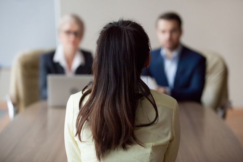 Businesswoman and businessman HR manager interviewing woman. Candidate female sitting her back to camera, focus on her, close up rear view, interviewers on background. Human resources, hiring concept. engineer job interview
