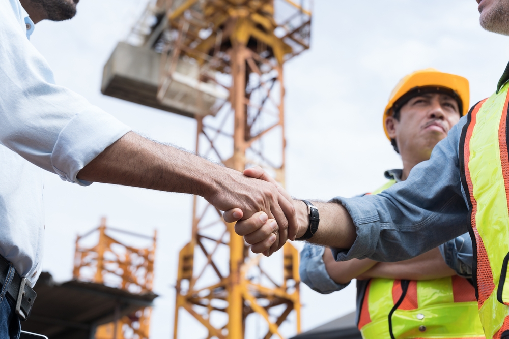 Team of male engineers in safety vests shake hands