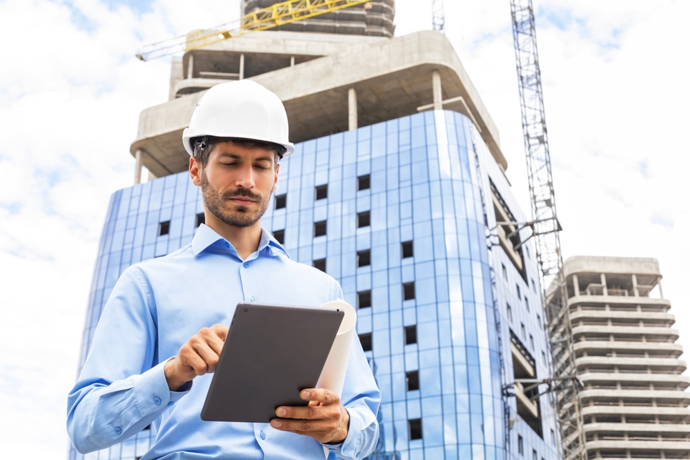Engineer man in helmet use tablet computer for controls construction of skyscrapers, background buildings under construction