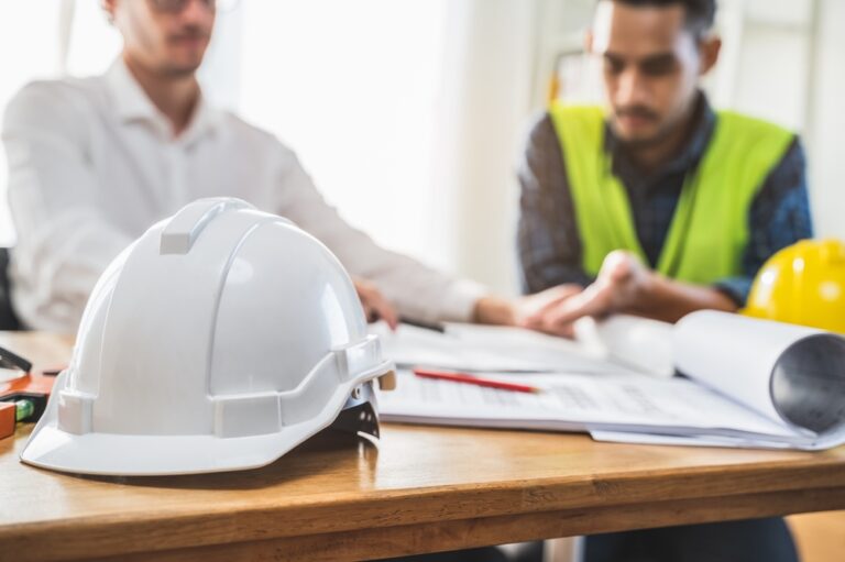 Close up white safety helmet on the table and engineers discuss plans and documents