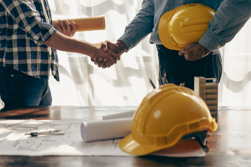 Engineers shaking hands in hiring meeting, holding hard hats and blueprints