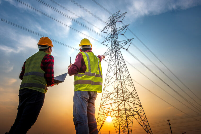 Picture of two electrical engineers using a notebook computer standing at a power station to view the planning work by producing electrical energy at high voltage electrodes