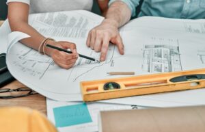 Blueprint, architecture and hands of people at desk with planning, support and project management. Writing notes, collaboration and design team in office for ideas, civil engineering and drawing
